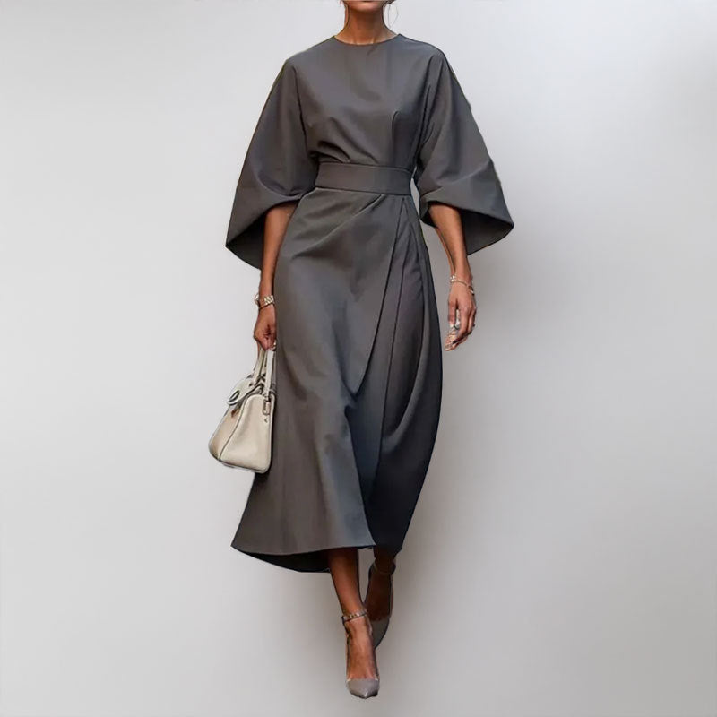 Female wearing an elegant draped maxi dress with satin-like texture on a plain background.