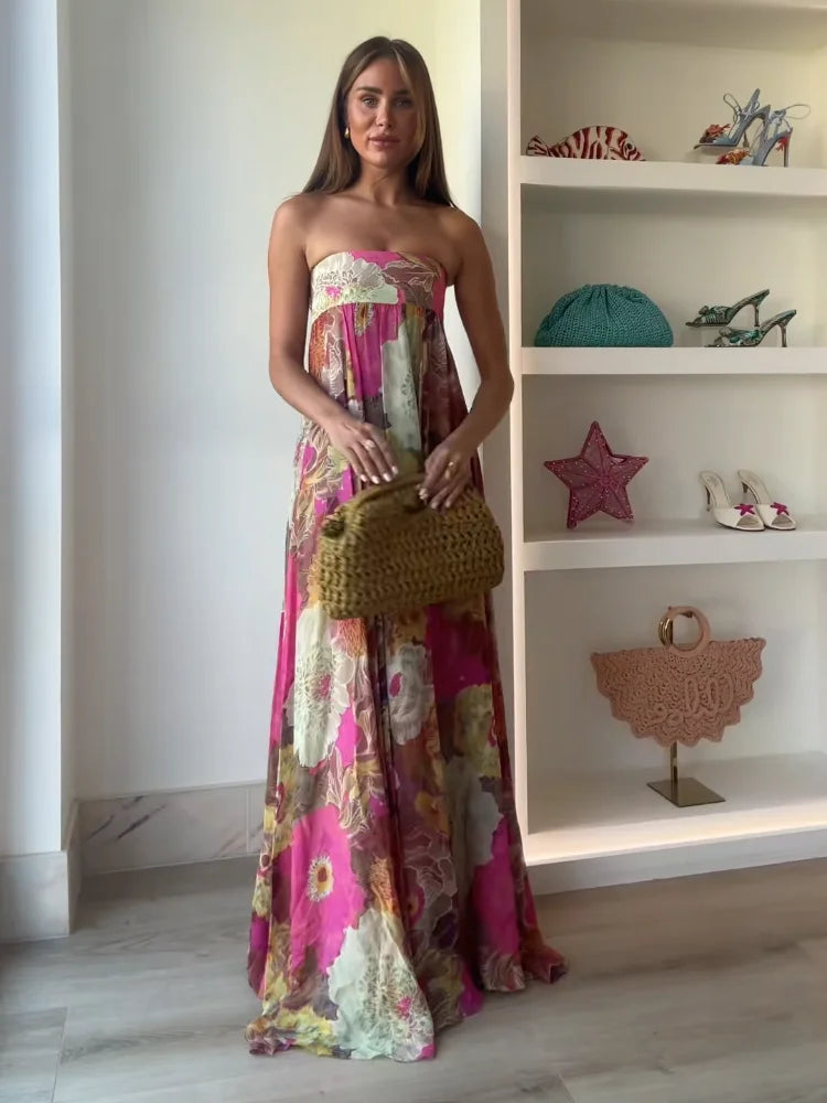Female model in flowing floral maxi dress on plain background.