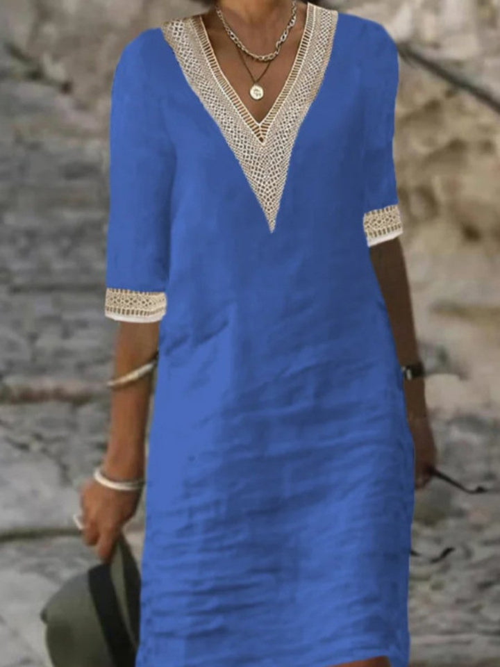 Model in a relaxed fit midi dress with lace trim standing near a natural stone wall.
