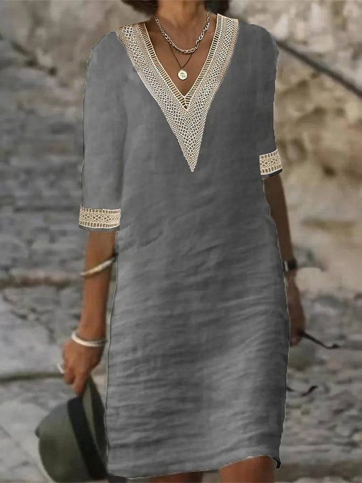 Female wearing an elegant V-neck midi dress with 3/4 sleeves by a nature stone wall.