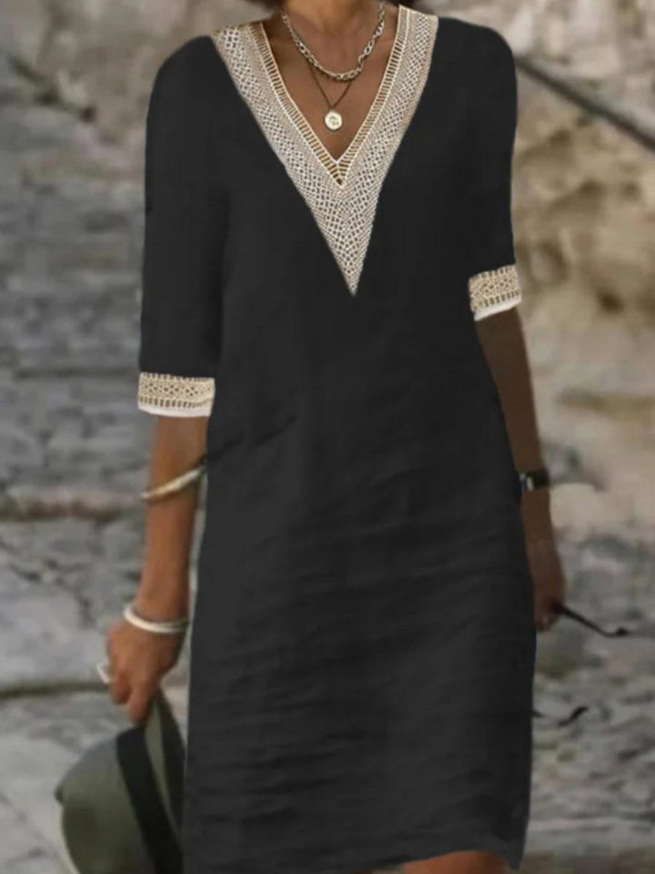 Woman styling a lace trim midi dress with a soft outdoor stone wall background.