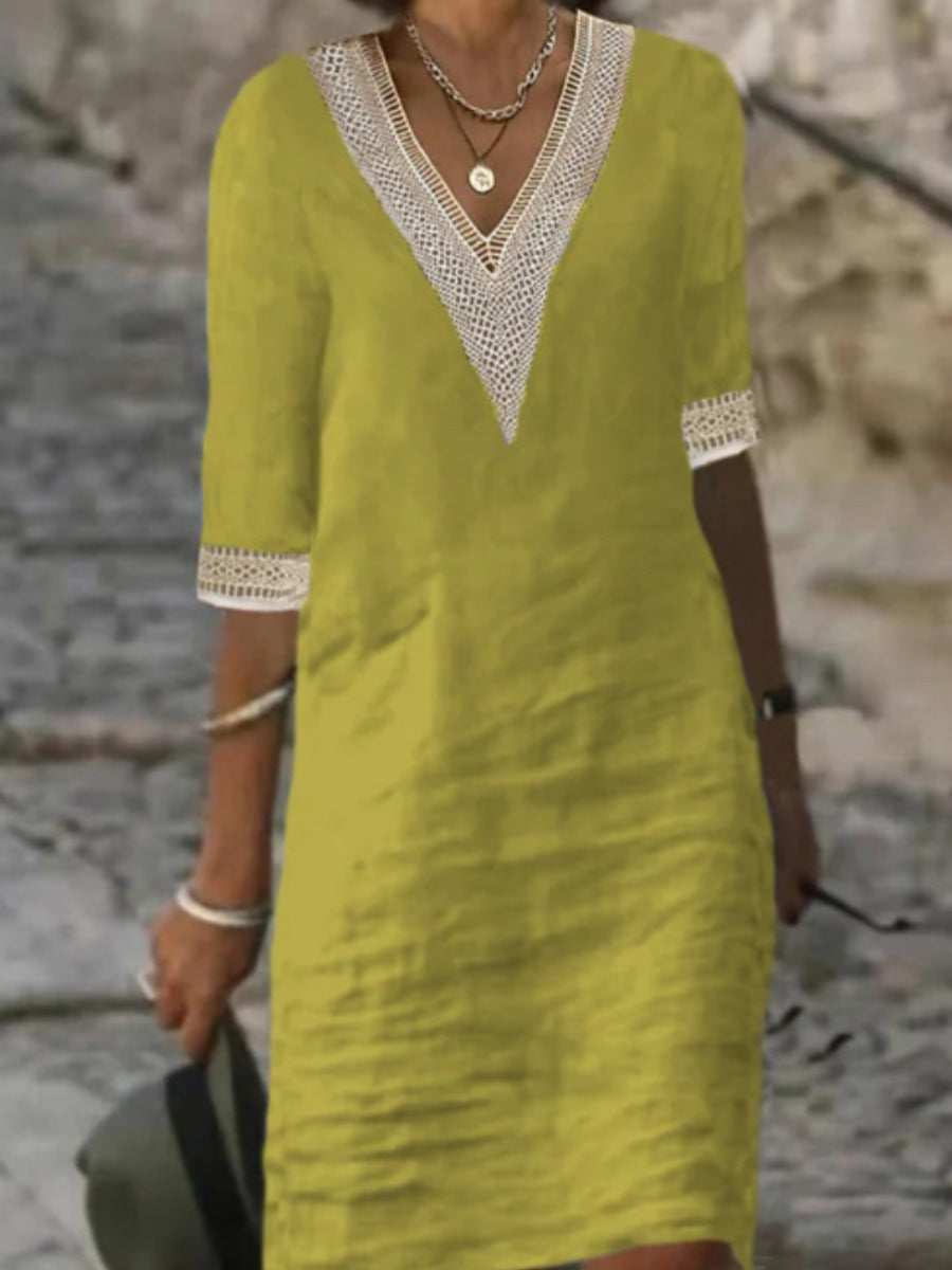 Woman wearing a casual elegant midi dress with V-neckline near a nature wall stone background.