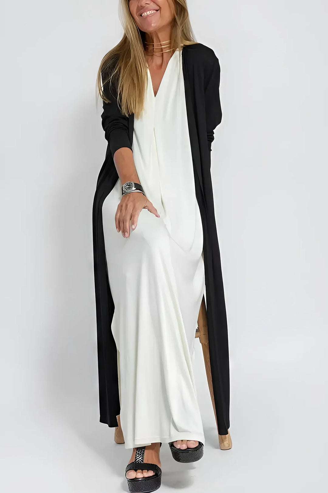 Timeless flowing dress w/ model on a plain background, featuring simple refined details.
